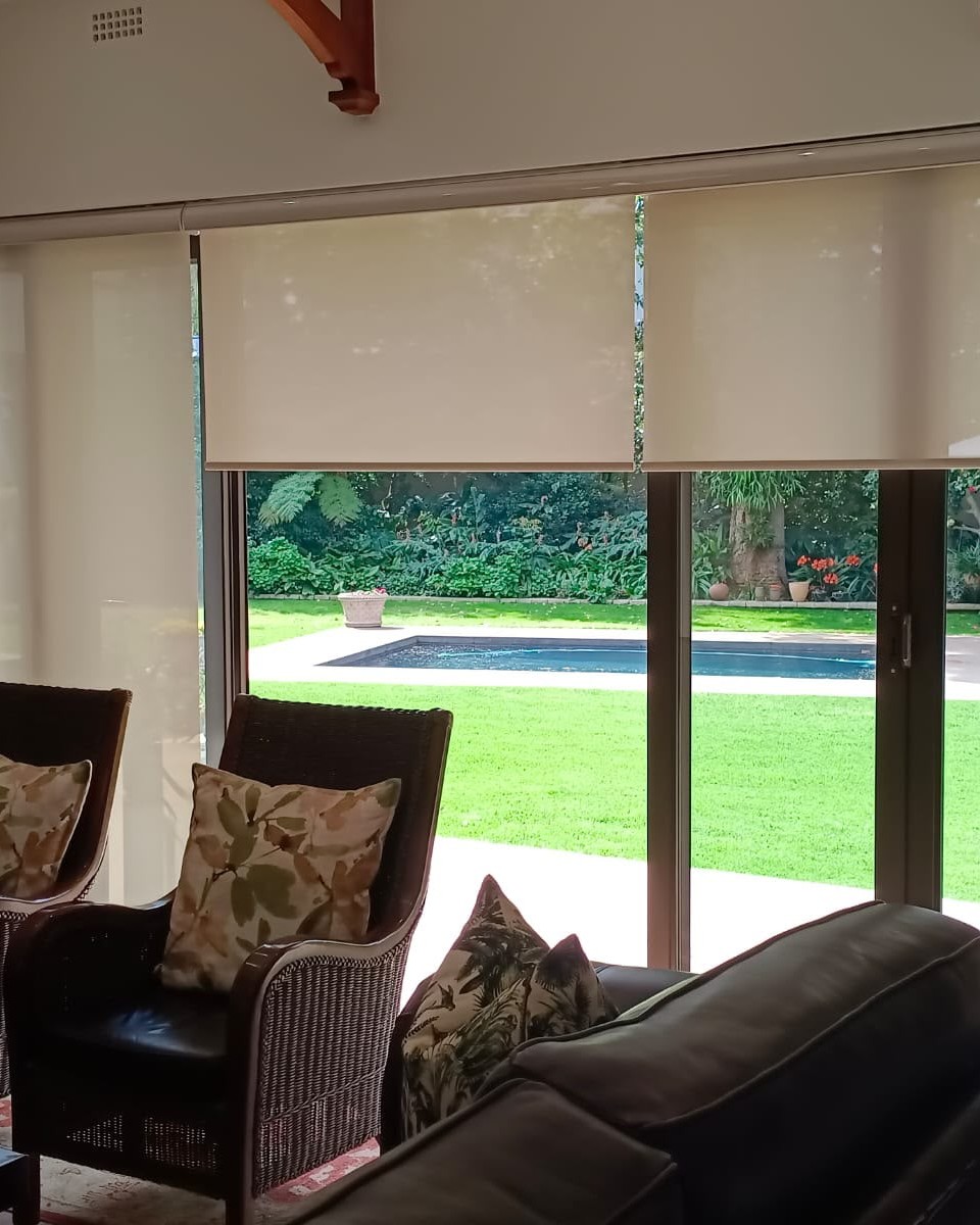 Elegant roller blinds fitted over sliding doors overlooking a lush garden and swimming pool